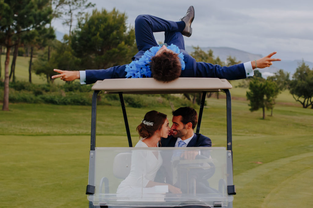 Novios en un carrito de golf con un amigo tumbado en el techo, boda en la Real Sociedad de Golf de Neguri